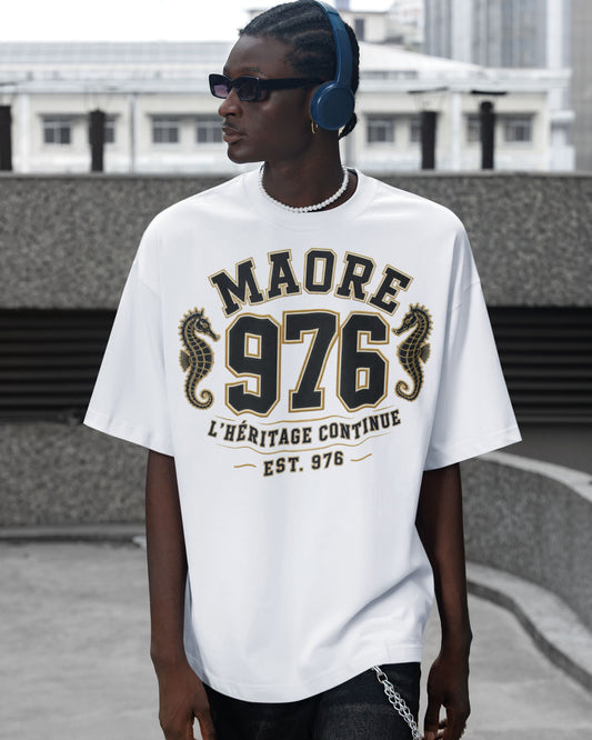 Homme portant un t-shirt blanc oversize WASI « MAORÉ 976 – L'Héritage Continue » avec deux hippocampes dorés, dans un décor urbain contemporain mettant en valeur la coupe et le design du vêtement.
