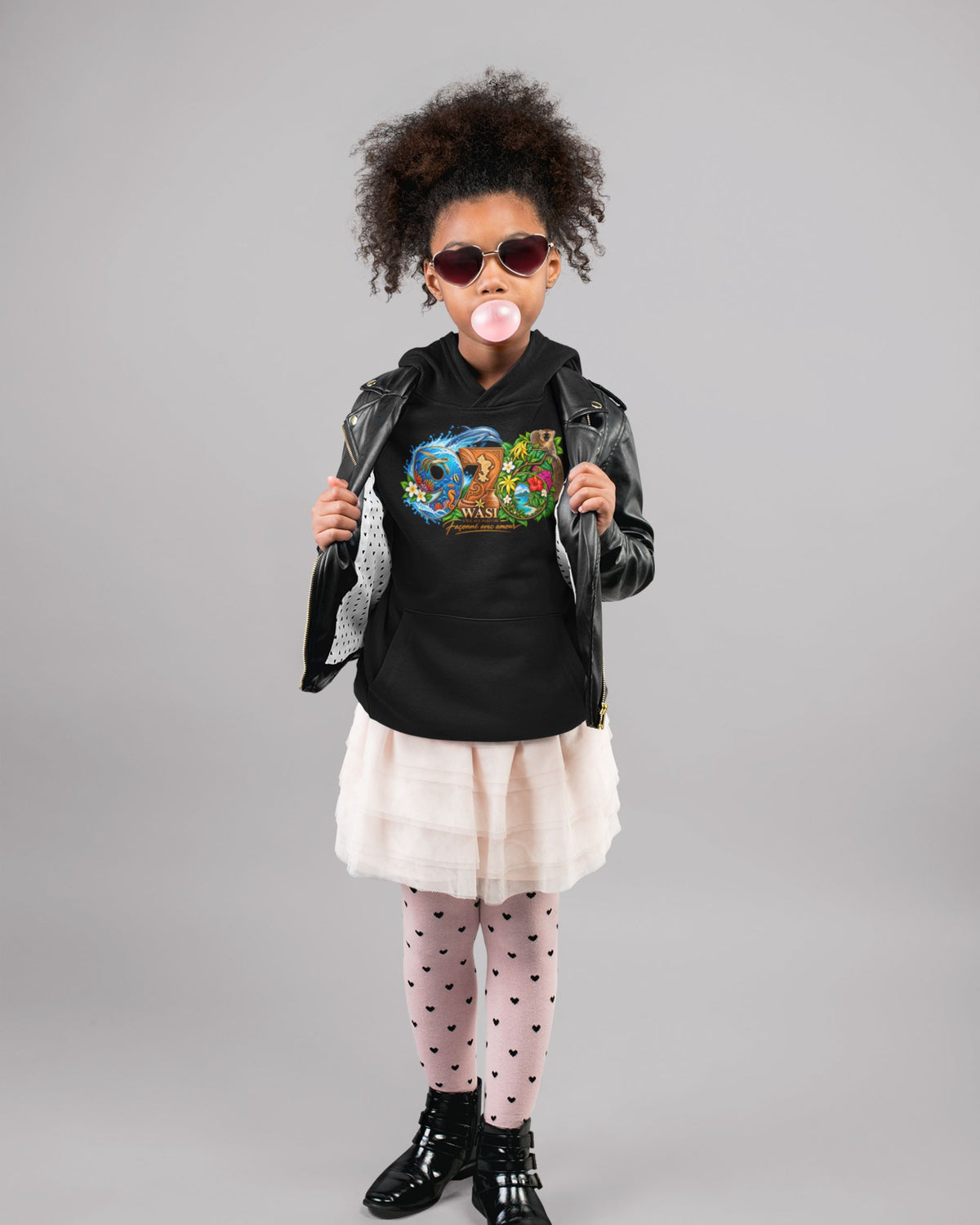 Enfant en pied portant le sweat à capuche noir WASI 976 avec une veste noire, une jupe claire et des lunettes de soleil.