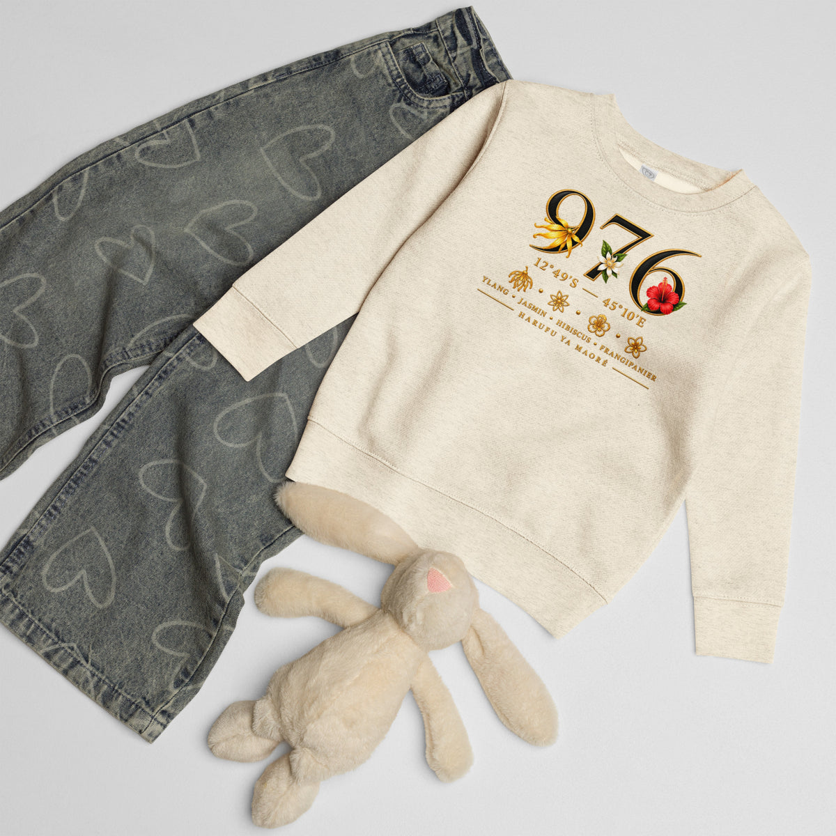 Sweat enfant écru chiné au motif 976 fleuri, présenté à plat avec un jean gris à motifs de cœurs et une peluche lapin beige