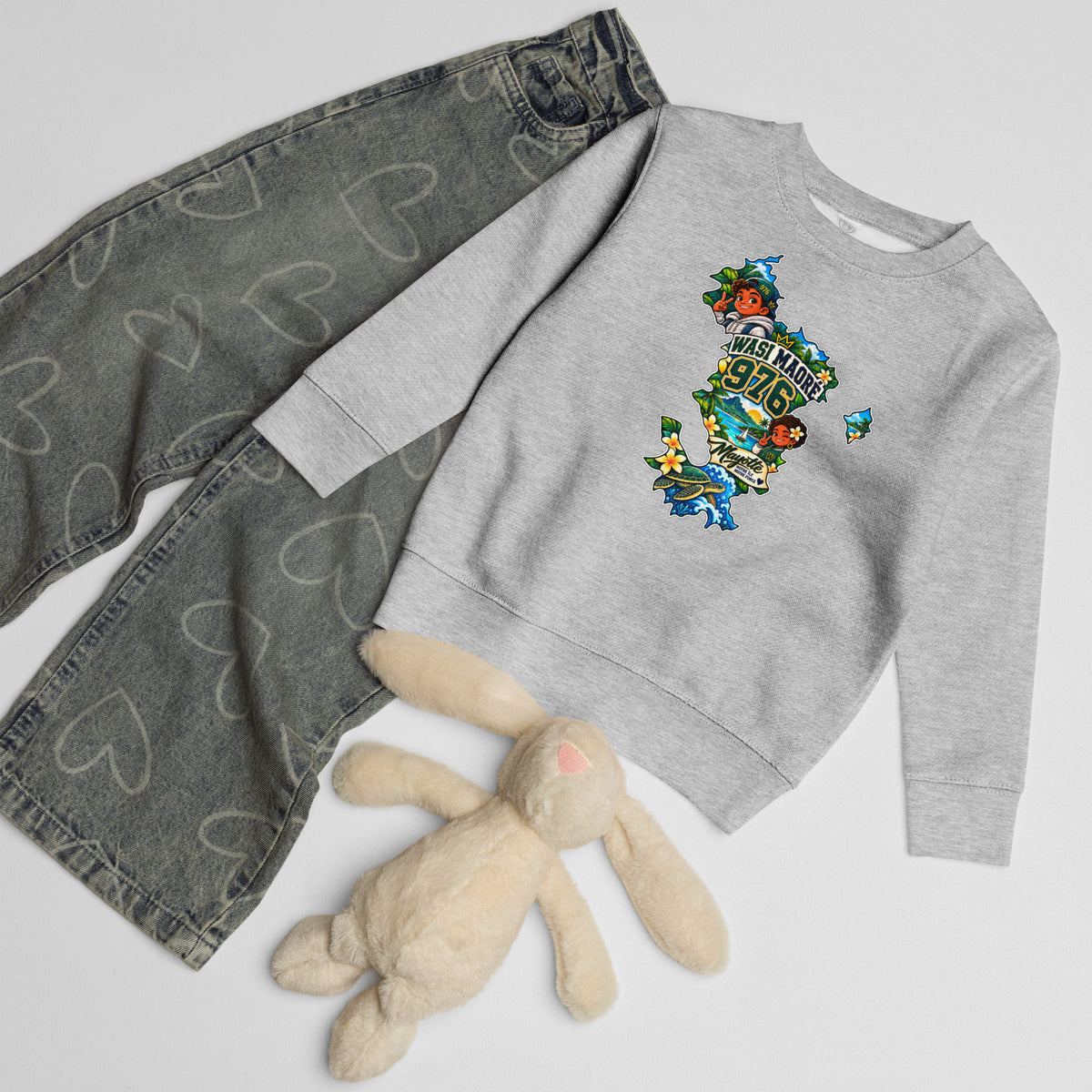 Sweat enfant gris chiné WASI Maoré 976 présenté à plat avec un jean gris à motifs de cœurs et une peluche lapin beige. 
