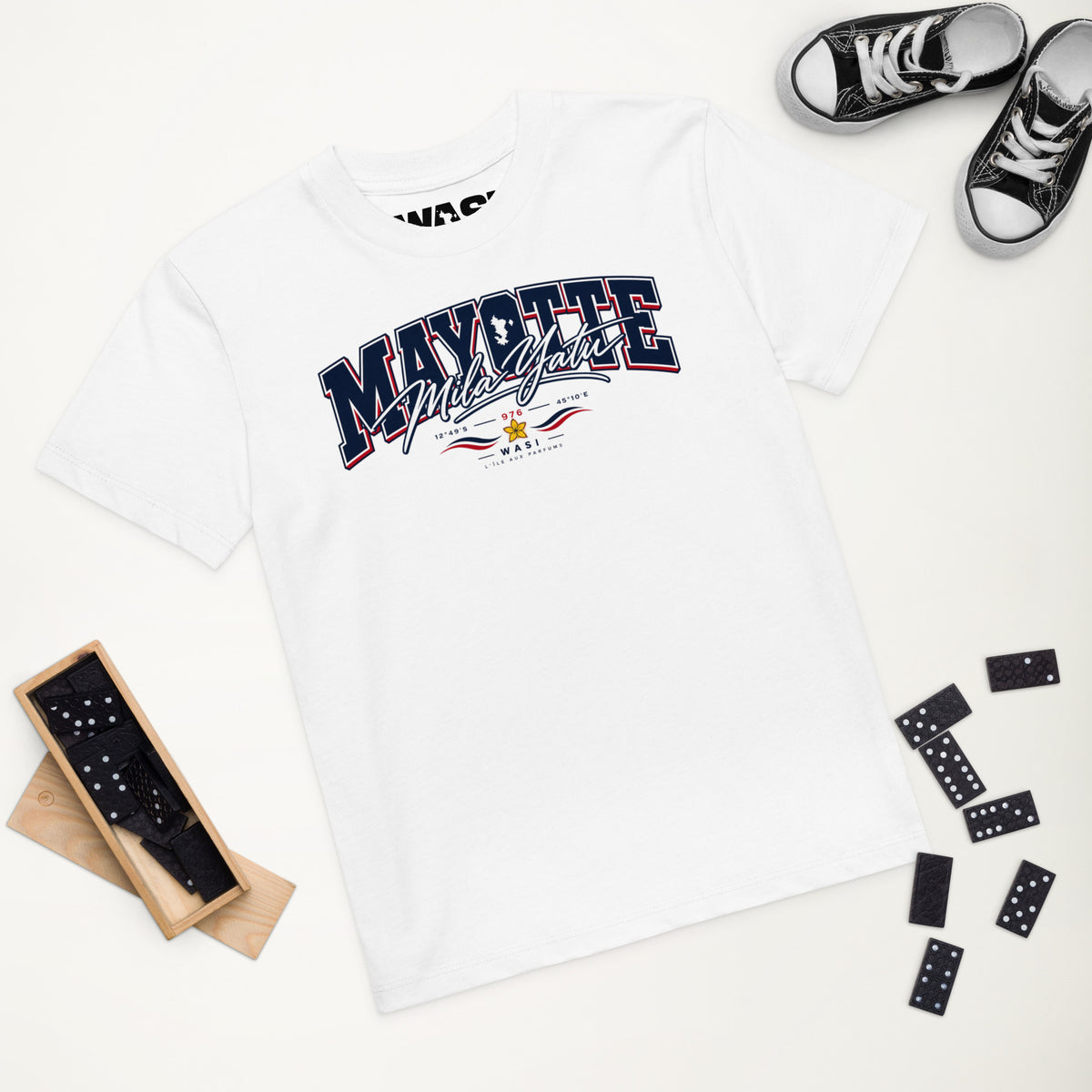 T-shirt enfant blanc Mayotte Mila Yatu présenté à plat, entouré de dominos noirs et de baskets noires et blanches.