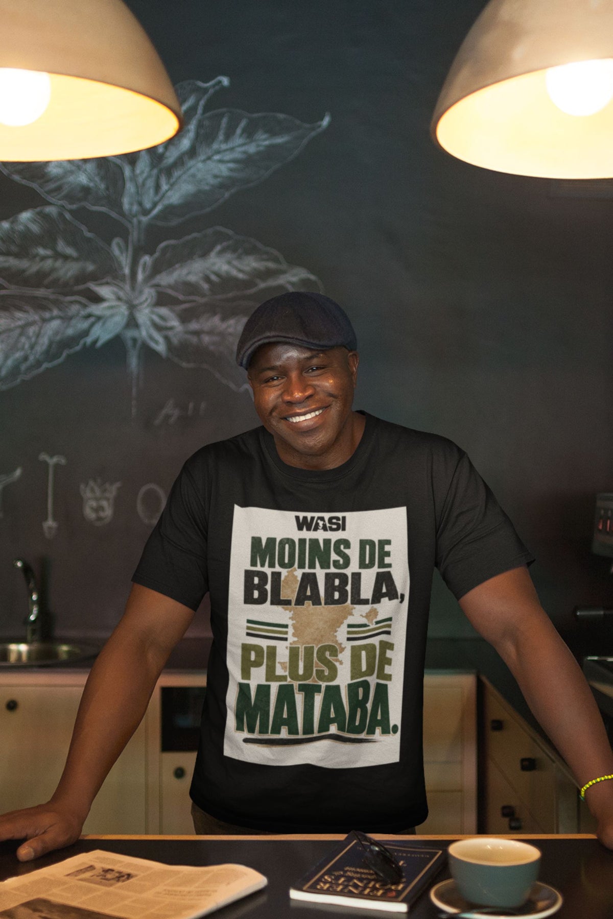 Homme portant le t-shirt noir WASI "Moins de blabla, plus de Mataba" dans un café, ambiance chaleureuse