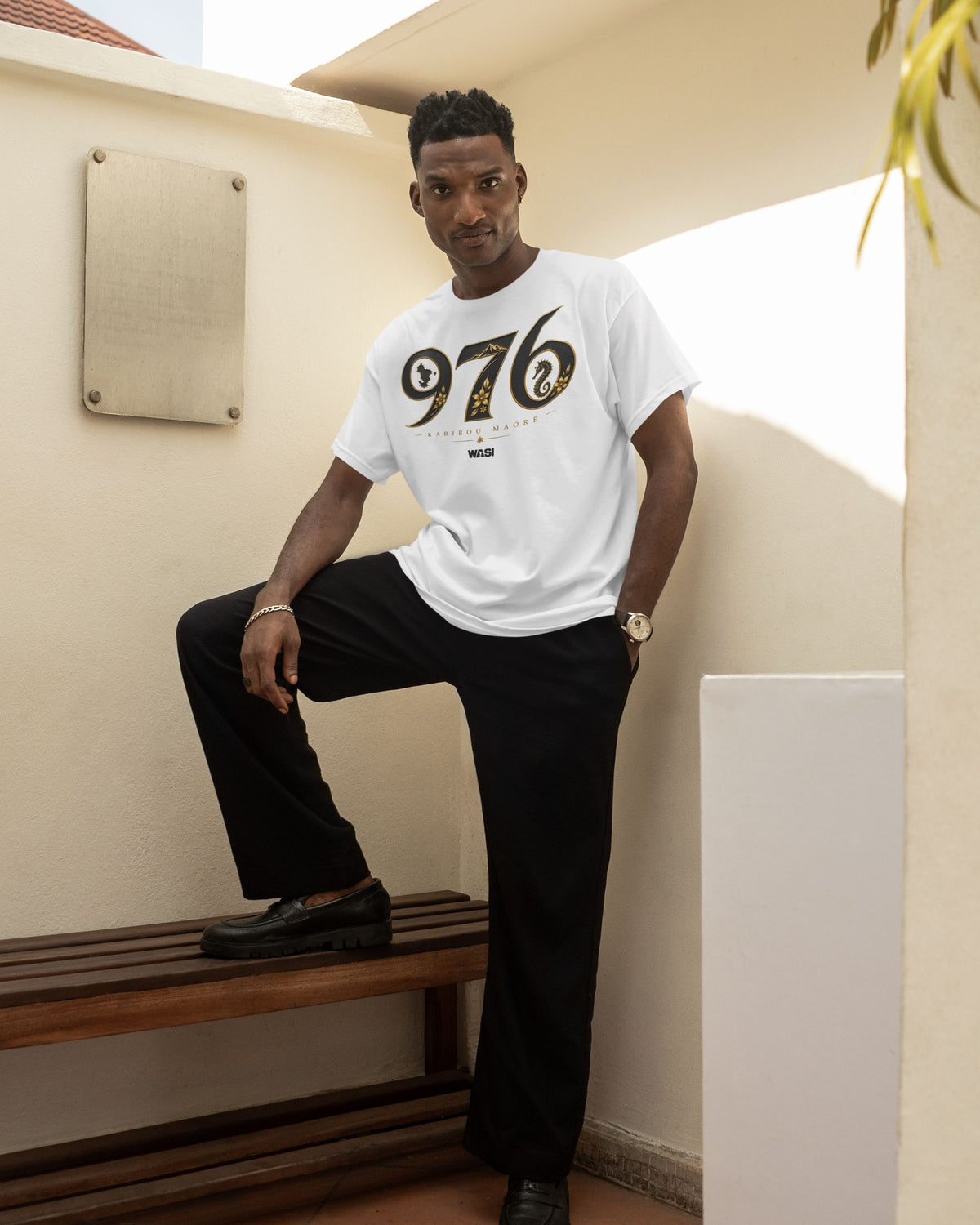 Homme portant un t-shirt blanc WASI Karibou Maoré 976 en 100 % coton, vêtement streetwear inspiré des symboles emblématiques de Mayotte, photographie lifestyle en extérieur.