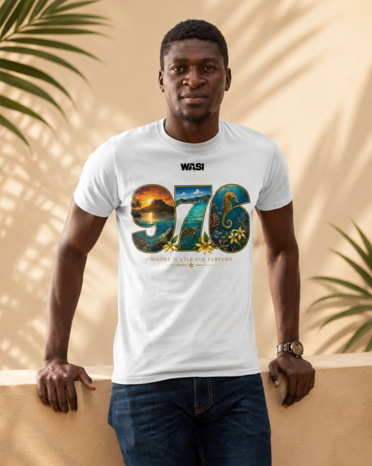 Homme portant un t-shirt blanc WASI « 976 Lagon Maoré » avec un design inspiré du lagon de Mayotte, photographié devant un décor tropical aux tons sable et aux ombres de palmiers.