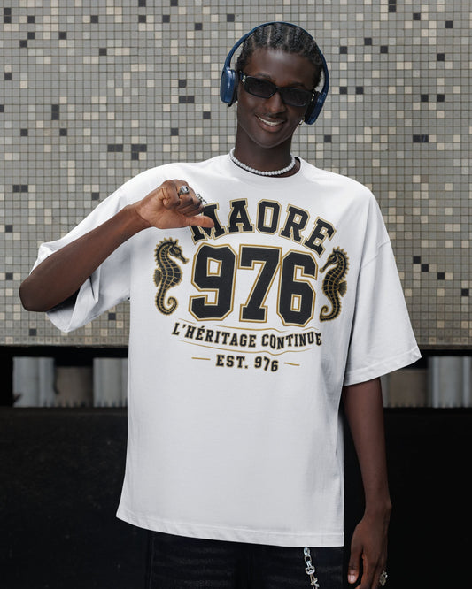 Homme portant un t-shirt blanc oversize WASI « MAORÉ 976 – L'Héritage Continue », avec deux hippocampes dorés et un design inspiré du patrimoine de Mayotte, photographié en milieu urbain.
