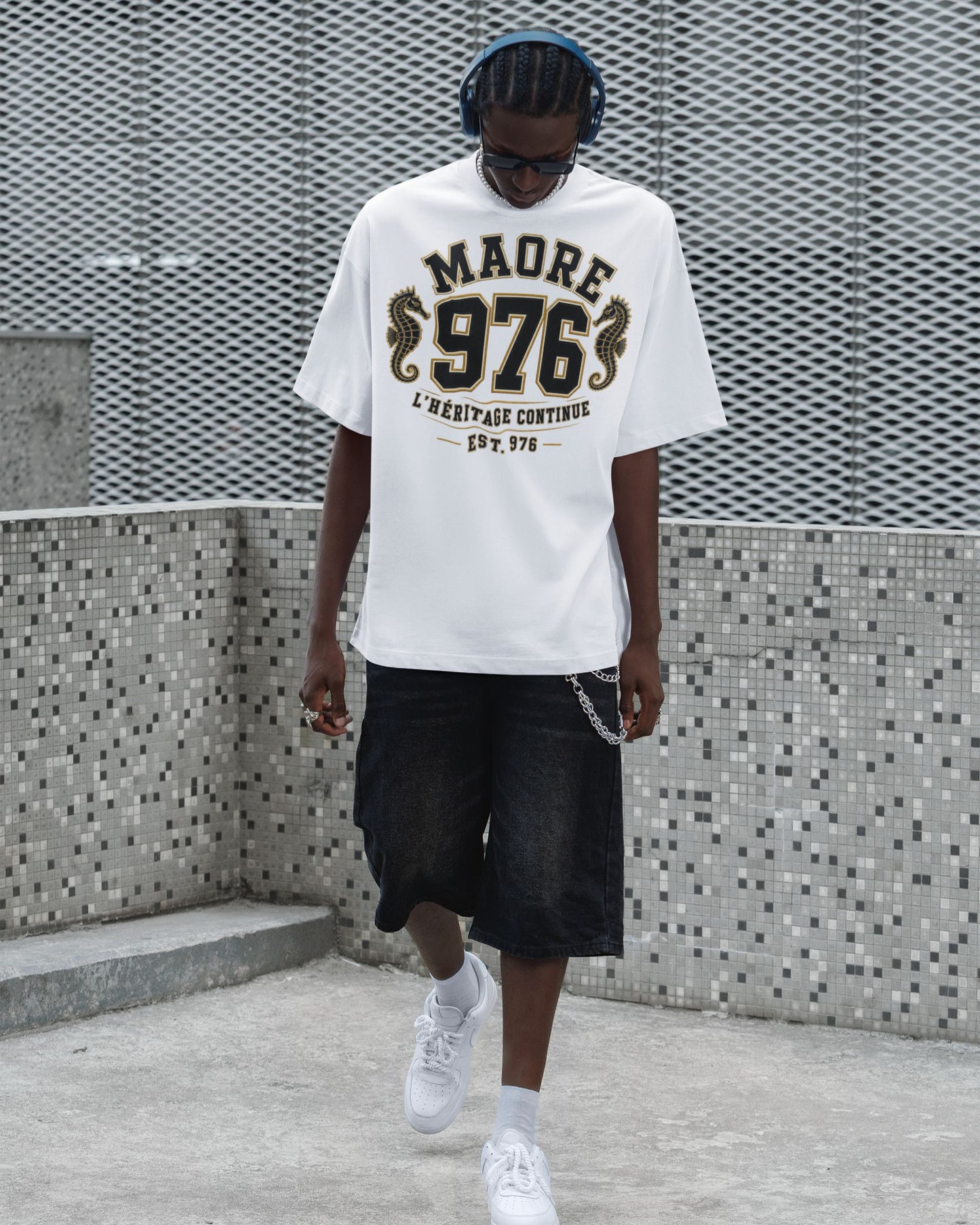 Homme portant un t-shirt blanc oversize WASI « MAORÉ 976 – L'Héritage Continue » avec deux hippocampes dorés, photographié dans un décor urbain moderne inspiré du streetwear.