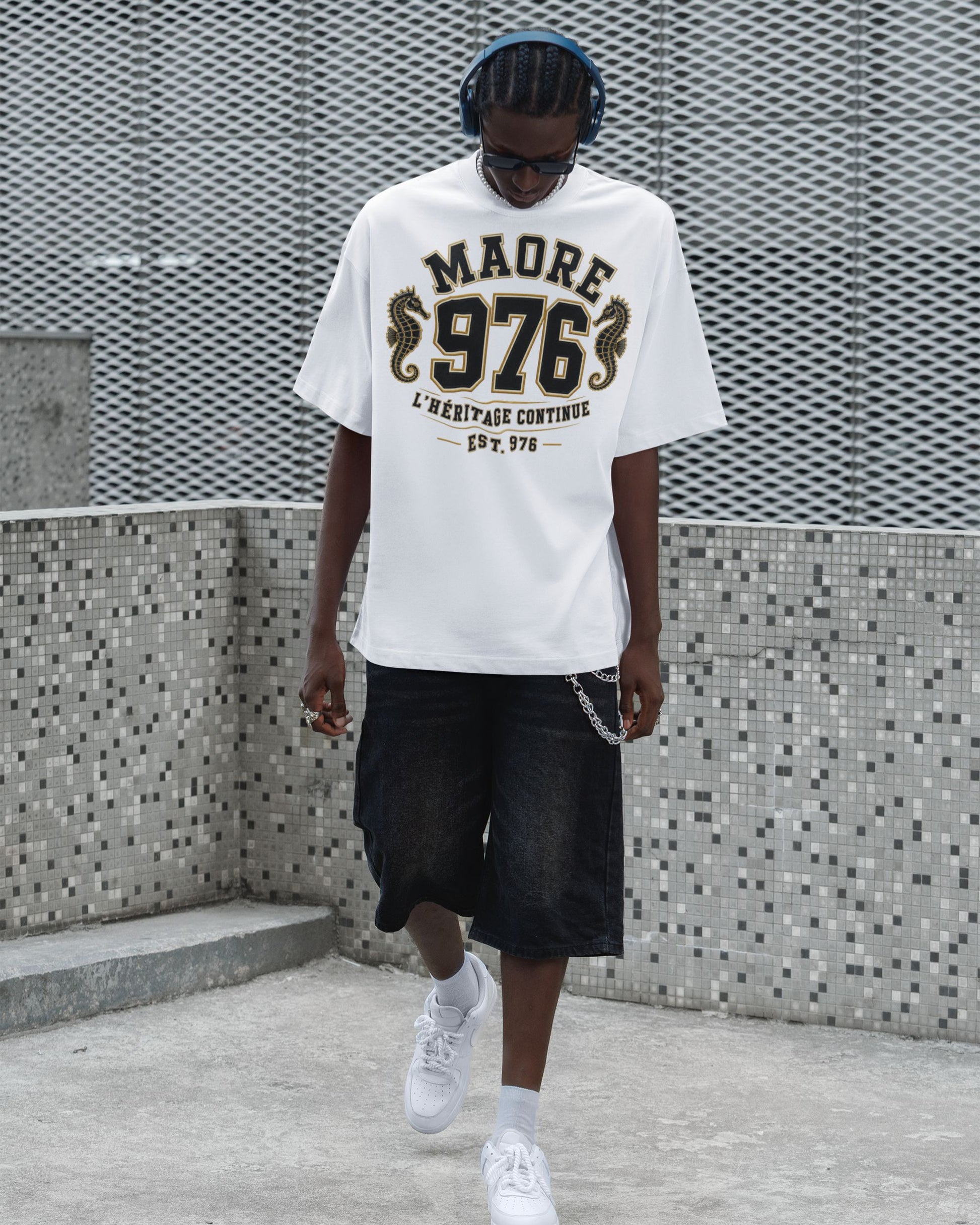Homme portant un t-shirt blanc oversize WASI « MAORÉ 976 – L'Héritage Continue » avec deux hippocampes dorés, photographié dans un décor urbain moderne inspiré du streetwear.