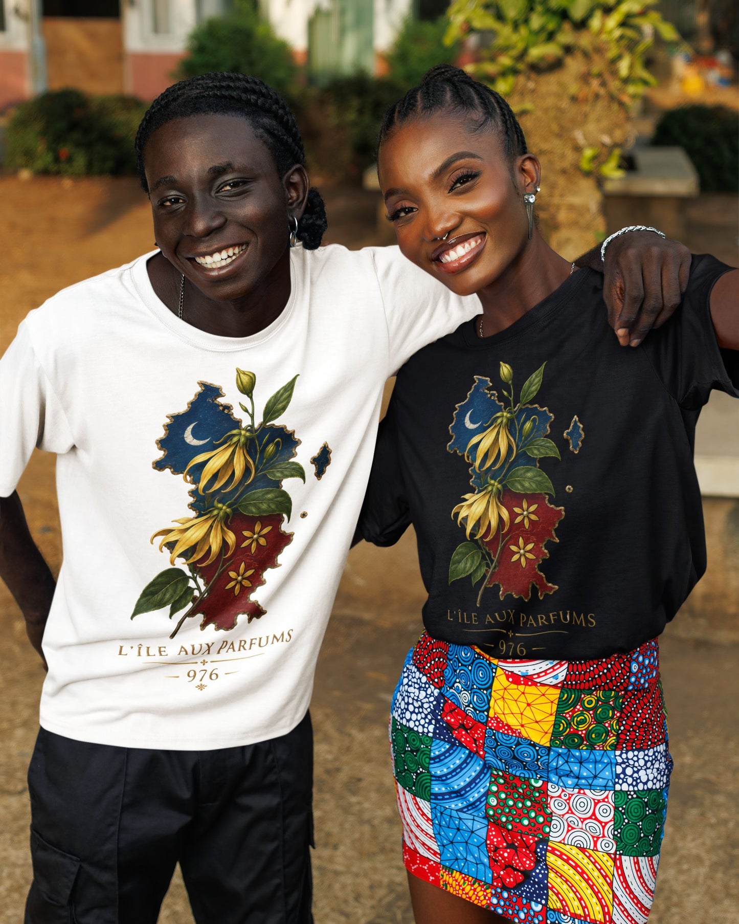 Deux personnes portant des t-shirts WASI L'Île aux Parfums 976 en coton, disponibles en blanc et noir, avec illustration de la carte de Mayotte et de fleurs d'ylang-ylang, photographie lifestyle en extérieur.